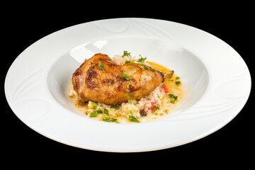 Delicious roasted chicken leg with vegetable risotto on a white plate, isolated on black background