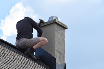 Roofer construction worker repairing chimney on grey slate shingles roof of domestic house, blue...