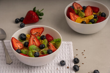 White bowl full of fruit salad on the table at kitchen surrounded by strawberries and blueberries