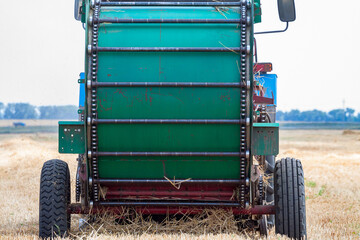 A tractor with a trailed bale making machine collects straw rolls in the field and makes round...