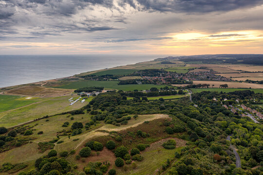 Aerial view of Muckleburgh Hill and Weybourne in Norfolk, the sun rising above Sheringham in the distance complex grey clouds drift out over the sea
