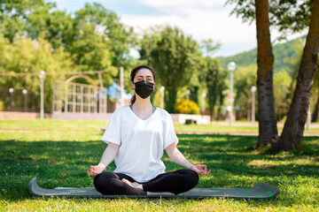 Fototapeta premium Yoga. A young woman in sports clothing and a medical mask, lying in the Park on the grass and meditating. The concept of healthy lifestyle and protection from viruses