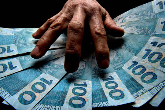 Notas de cem reais brasileiros e m&atilde;o de homem no escurid&atilde;o