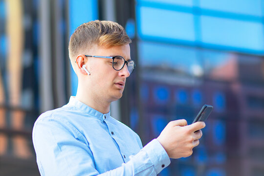 The student typing a message, a handsome European man sending an SMS message, sends SMS to his mobile smartphone. Serious young businessman businessman man in glasses, looks at his mobile phone.