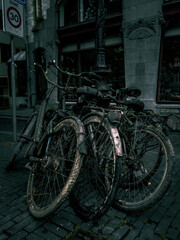 Amsterdam, the Netherlands - moody cold and dark street photowalk. Old rusty bikes just taken out from water of city canal parked and chained to the lamp post in the street. Moody cold tones look 