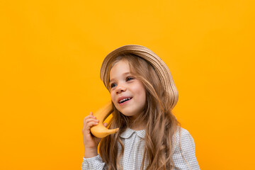 Pretty caucasian girl with hat holds gesticulates with banana isolated on yellow background