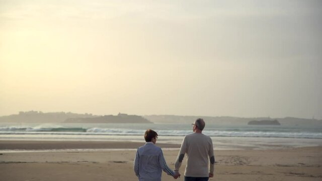 Couple in love walk by the beach at sunset holding hands 