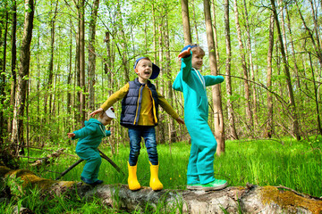 Naklejka na ściany i meble Children in the spring forest walk on a log. Hiking, camping, family outdoor activities. Friendship since childhood. A happy family with three children.