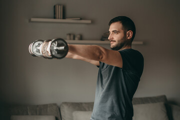 beautiful man doing exercises for biceps hands with metal dumbbells. Sport in quarantine at home. 