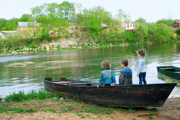 Three children in a boat on the river Bank looking into the distance, rear view.