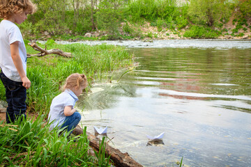 Children launch paper boats into the river. Brother and sister on the shore of the reservoir. Outdoor recreation, Hiking, camping. Children's games in the water.