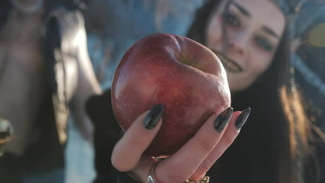 The witch holds out his hand with a red Apple at the forbidden fruit, close-up.