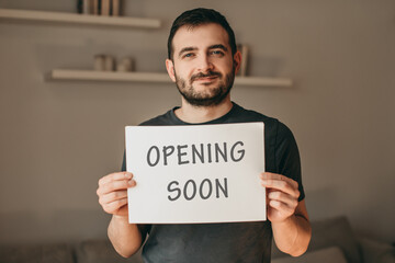 Happy man holding sign with inscription opening soon in cafe, restaurant, shop. Quarantine, coronavirus, isolation.