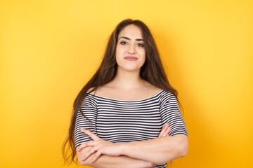 Waist up portrait of beautiful young female with positive expression, has crossed arms, feels happy and confident, wears casual clothes, isolated over gray background