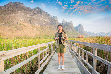 Fototapeta na wymiar Asian hikers carry heavy backpacking on a small Pavilion outdoor hiking path on a wooden bridge in a swamp with meadows with a blue mountain background. Khao Sam Roi Yot National Park