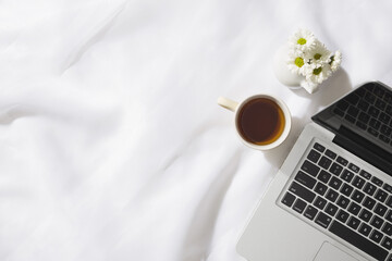 Top view of morning scene in voile fabric background with a notebook, mug of tea and a vase of white flowers with space for text.