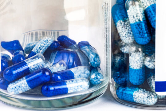 Lots of blue-white pills, transparent tablets with granules in a see through bottle containers seen from the side, macro, closeup. Medication, drugs, medicines and supplementation abstract concept