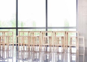 Many empty wooden stools near a table in a corporate lobby area, luch room, calm business canteen, no people, nobody. Vacant seats at company lunchroom with huge windows, abstract interior background