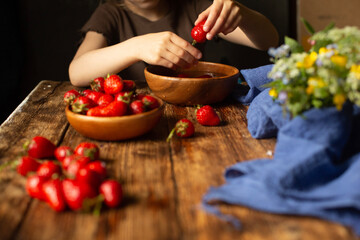 A child sits at a wooden table washes and eats strawberries.
