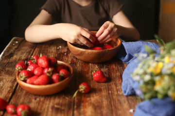 A child sits at a wooden table washes and eats strawberries.
