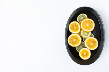 fresh and juicy sliced lemon and lime slices in water, in a black bowl on a white background, citrus background. beauty and health concept.