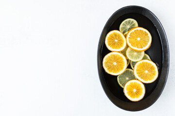 fresh and juicy sliced lemon and lime slices in water, in a black bowl on a white background, citrus background. beauty and health concept.