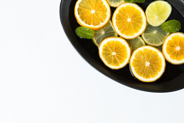 fresh and juicy sliced lemon and lime slices in water, in a black bowl on a white background, citrus background. beauty and health concept.