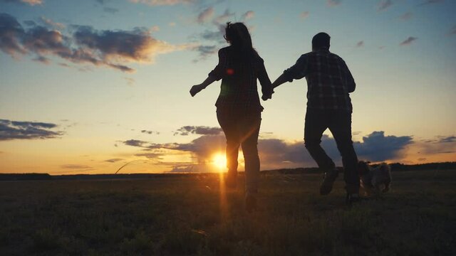 happy family couple and dog runs hands at sunset on a hilltop. concept of team business concept travel freedom victory happiness teamwork. happy family parents hold hands run in the rays of sunlight