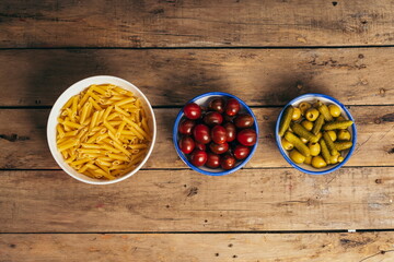 Ingredients for a pasta salad on an old wooden table, tomatoes, olives, pickles, crab sticks, onion and macaroni