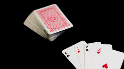 Obraz premium Ángulo levemente elevado de un juego de ases de poker aislados sobre un fondo negro y con iluminación directa sobre ellos. Junto se encuentra un mazo de cartas de fondo rojo. 