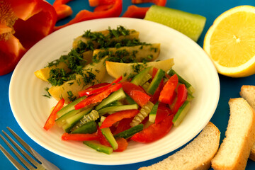Potatoes with greens and vegetable salad on a white plate. Blue background..