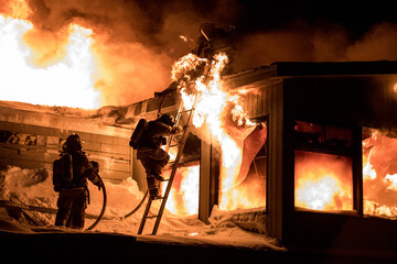 Huge fire blazing in commercial building and firefighter on a roof in winter condition.