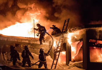 Huge fire blazing in commercial building and firefighter on a roof in winter condition.