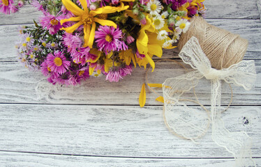 Bouquet of bright purple and yellow autumn flowers, a spool of thread and a bow made of a lace ribbon on a gray wooden background (with copy space for your text, selective focus) as a rustic backgroun