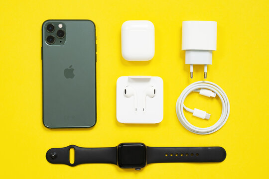 May 01, 2020, Rostov, Russia: Mobile phone iPhone, wireless headphones AirPods in box with case, Apple Watch S4 with sport band, USB Lightning Cable and power adapter on yellow background, top view.