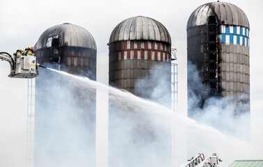 Firefighters battle silo fire. They spray water from the ladder basket. © Steve