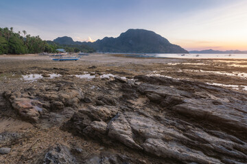 Palawan island, Philippines. El Nido village and mountain at sunset with rocky coastline by low tide in foreground