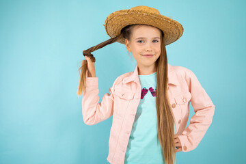 portrait of a charming beautiful young girl with a straw hat on her head twisting her hair in her hand on a blue background