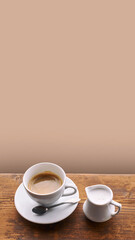 Coffee with milk in ceramic cup with small milk jug on old wooden window sill background