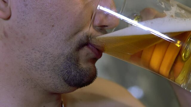 Untidy. unshaven man drinks beer from a transparent mug at home