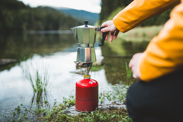 Human hand holding geyser coffee maker while preparing tea or coffee on camping gas stove by the...