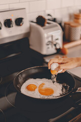 Breakfast preparation. Making morning meal. Weekday routine. Cooking food before work for family. Cracking the eggs into the pan. Home lifestyle. Brunch with husband. Stove, toaster. Selective focus