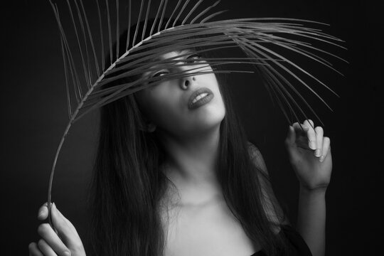 black and white portrait of a young woman with leaf palms. Studio photo