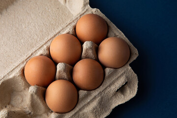Close up view of raw chicken eggs in an egg box on a blue background