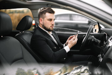 Handsome caucasian businessman driver inside in vehicle  with coffee and gadget and check mail and talking with partners