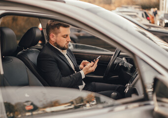 Handsome caucasian businessman driver inside in vehicle  with coffee and gadget and check mail and talking with partners