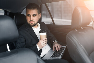 Handsome caucasian businessman driver inside in vehicle  with coffee and gadget and check mail and talking with partners
