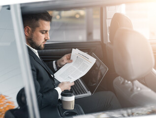 Handsome caucasian businessman driver inside in vehicle  with coffee and gadget and check mail and talking with partners