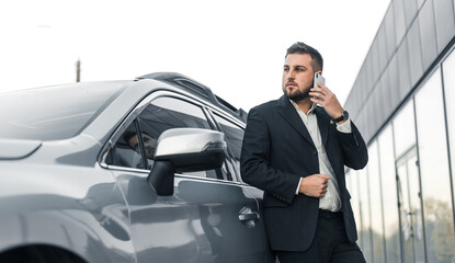 Handsome businessman with smartphone near vehicle on office parking