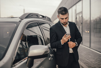 Handsome businessman with smartphone near vehicle on office parking